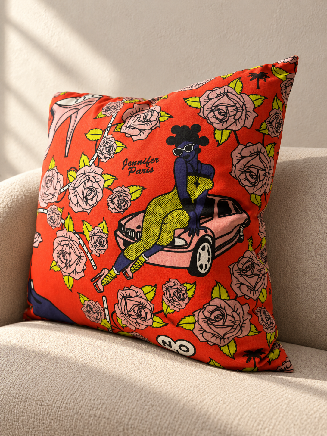 Jennifer Paris: Orange Shine Shine cushion with pink roses and an illustrated woman in sunglasses sitting on a car.