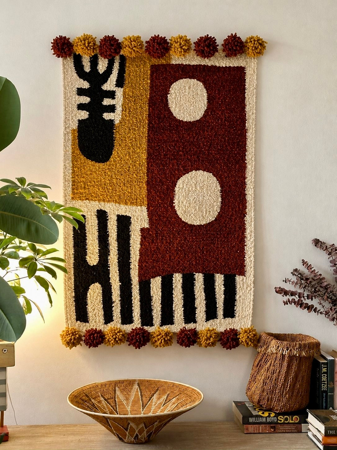 Handmade wool wall hanging with geometric colour-block design in rust, ochre and black, with pompom edging – Mopti Living