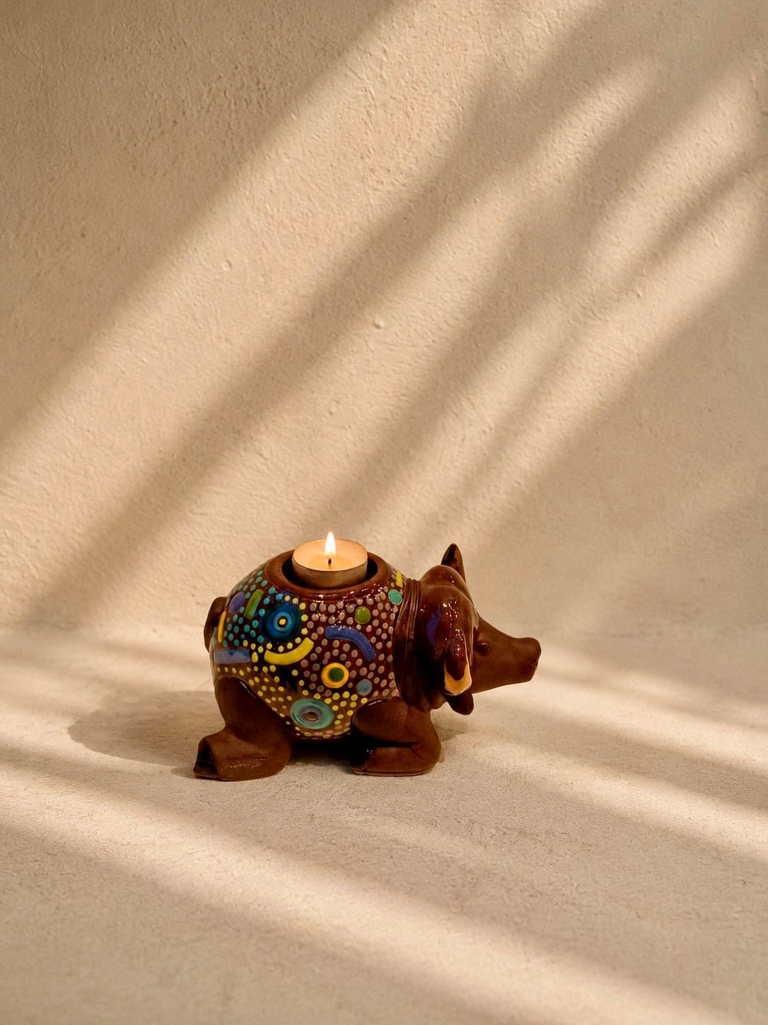 Decorative candle holder shaped like a buffalo with colorful designs on a beige background