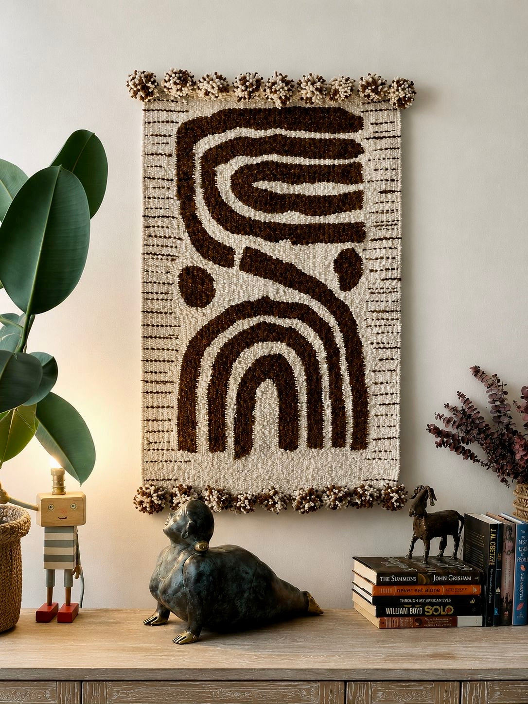 Handmade wool wall hanging with abstract curved lines and arch motif in dark brown on cream, with pompom edging – Mopti Living