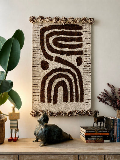 Handmade wool wall hanging with abstract curved lines and arch motif in dark brown on cream, with pompom edging – Mopti Living