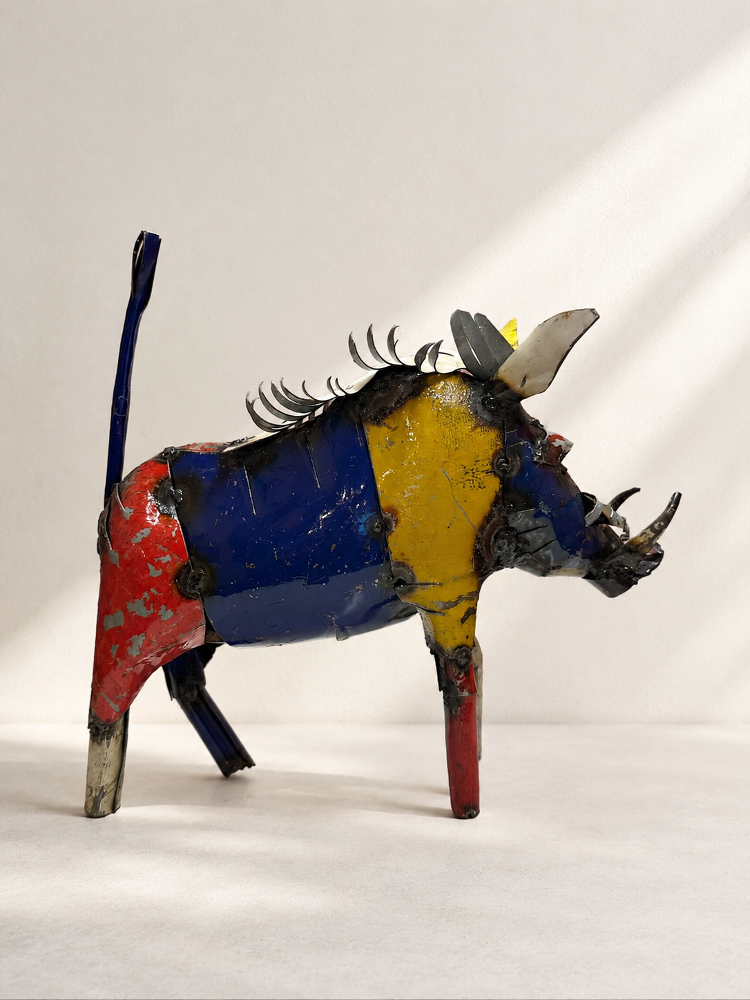 Handmade recycled metal warthog sculpture with colourful layered panels in red, blue, yellow and green — Mopti Living