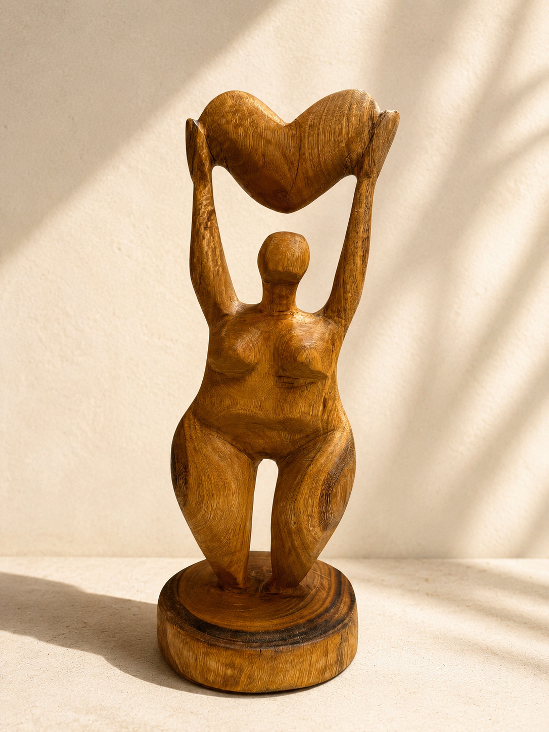 Hand-carved wooden sculpture of a woman with arms raised holding a heart overhead, standing on a round base — Mopti Living