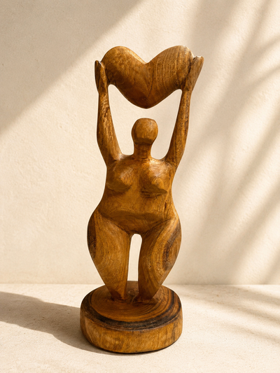 Hand-carved wooden sculpture of a woman with arms raised holding a heart overhead, standing on a round base — Mopti Living