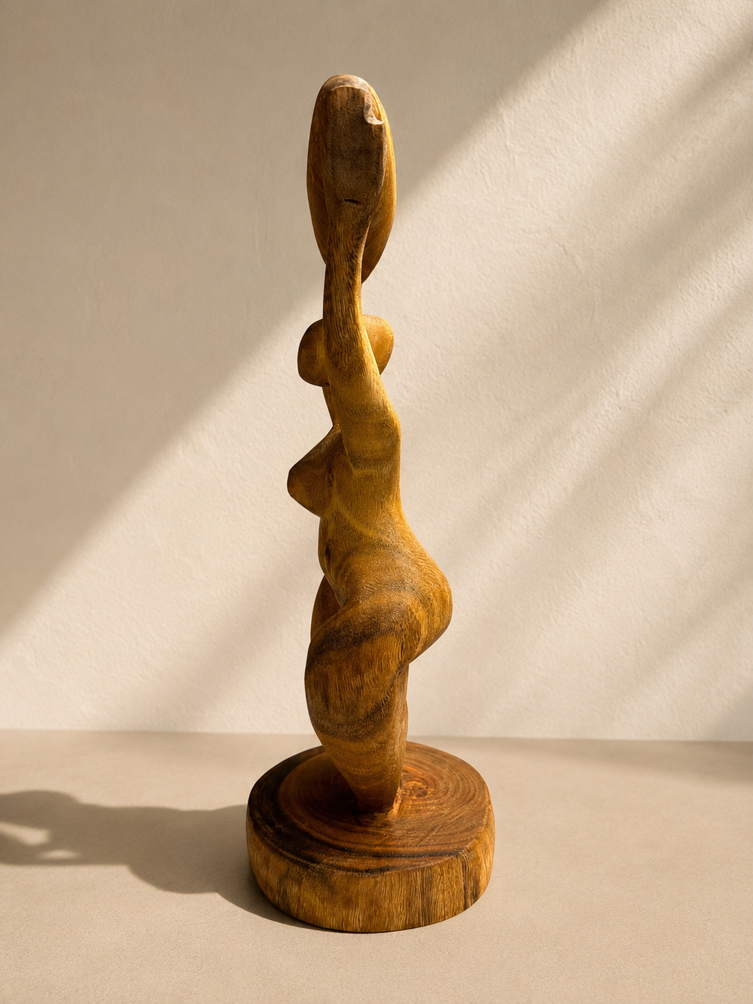 Hand-carved wooden sculpture of a woman with arms raised holding a heart overhead, standing on a round base — Mopti Living